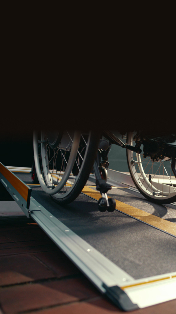 Rollstuhlfahrer steigt über eine seitliche Rampe vom Gehweg in einen Kia WAV ein.